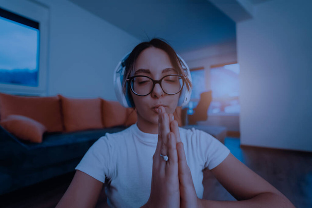 Una joven está practicando yoga y relajándose con auriculares en la cabeza en un apartamento moderno. - Foto, imagen