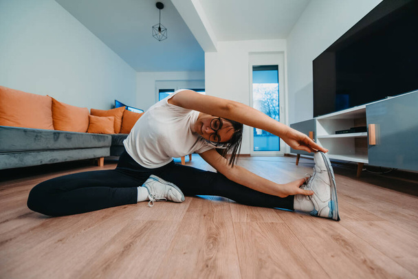 Egy nő nyújtózkodik a lakásában kora reggel edzés után, tükrözve elkötelezettségét az egészséges életmód iránt. Ez a pillanat rávilágít a rendszeres testmozgás és öngondoskodás fontosságára. - Fotó, kép
