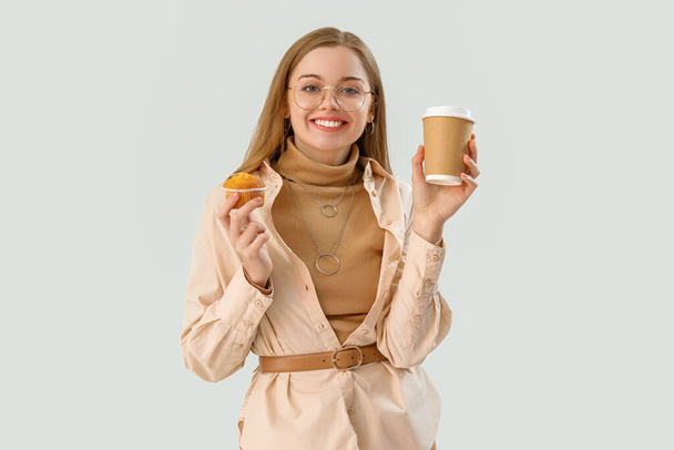 Young woman with tasty cupcake and cup of coffee on light background - Photo, Image