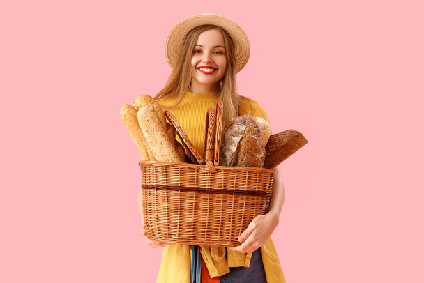 Mujer joven en sombrero con cesta de pan fresco sobre fondo rosa - Foto, imagen
