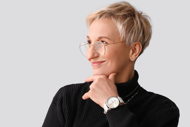 Thoughtful mature woman in eyeglasses on light background, closeup - Photo, Image