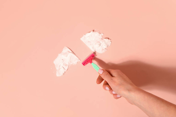 Mano femenina con afeitadora de seguridad y espuma de afeitar sobre fondo rosa - Foto, Imagen