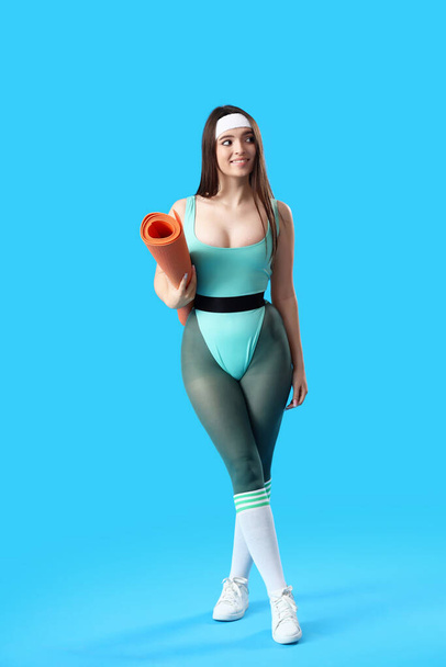 Sportieve jonge vrouw met yoga mat op blauwe achtergrond - Foto, afbeelding