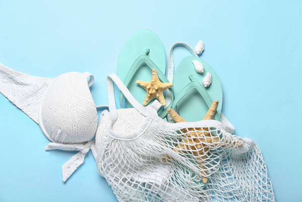 String bag with flip-flops, swimsuit and starfishes on blue background - 写真・画像