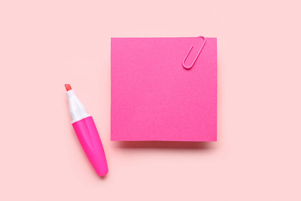 Nota adhesiva rosa con clip de papel y marcador sobre fondo de color - Foto, imagen
