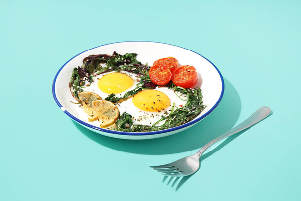 Plate with tasty fried eggs and salad on blue background - Фото, изображение