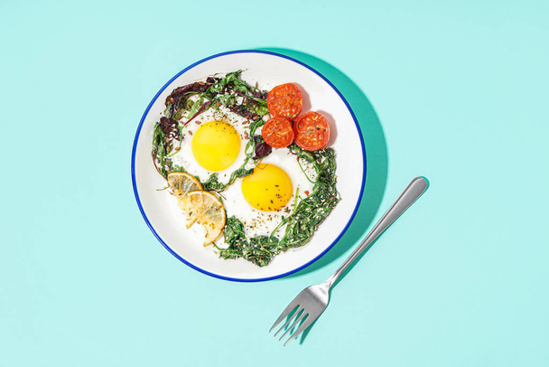 Prato com saborosos ovos fritos e salada em fundo azul - Foto, Imagem