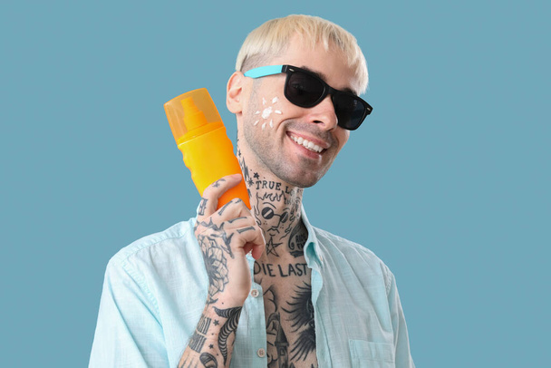 Tatuoitu mies aurinkovoiteella vaaleansinisellä taustalla - Valokuva, kuva