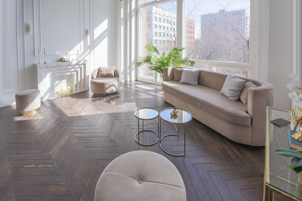 very light and bright interior of luxurious cozy living room with chic soft beige furniture with gold metallic elements, huge window to the floor and wooden parquet - Foto, Imagem