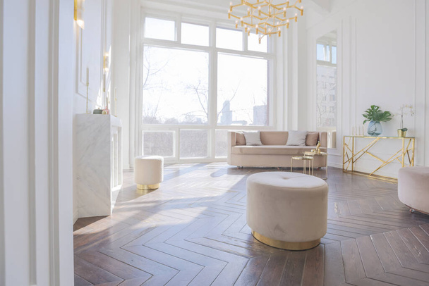 very light and bright interior of luxurious cozy living room with chic soft beige furniture with gold metallic elements, huge window to the floor and wooden parquet - 写真・画像