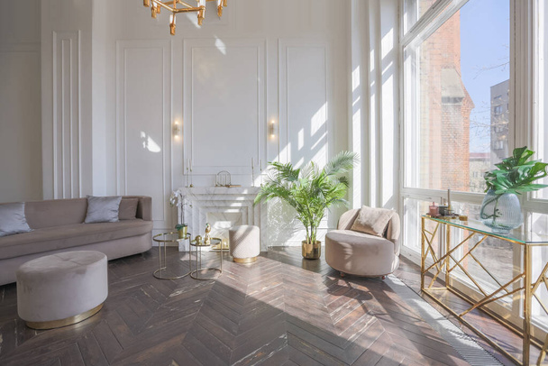 very light and bright interior of luxurious cozy living room with chic soft beige furniture with gold metallic elements, huge window to the floor and wooden parquet - Foto, afbeelding
