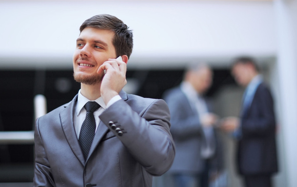 Businessman standing inside modern office building talking on a mobile phone - Φωτογραφία, εικόνα