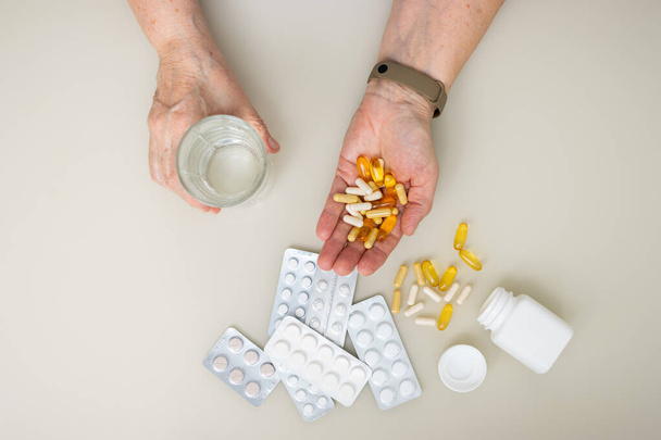Femme âgée avec de vieilles mains ridées à la table tenant différentes capsules et vitamines, palme pleine avec des pilules pour le traitement. Concept de soins de santé et de médecine, vue de dessus. - Photo, image