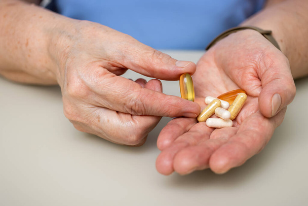 Femme âgée avec de vieilles mains ridées à la table tenant Omega 3 capsule, vitamines et diverses pilules pour le traitement. Concept de santé et de médecine. - Photo, image