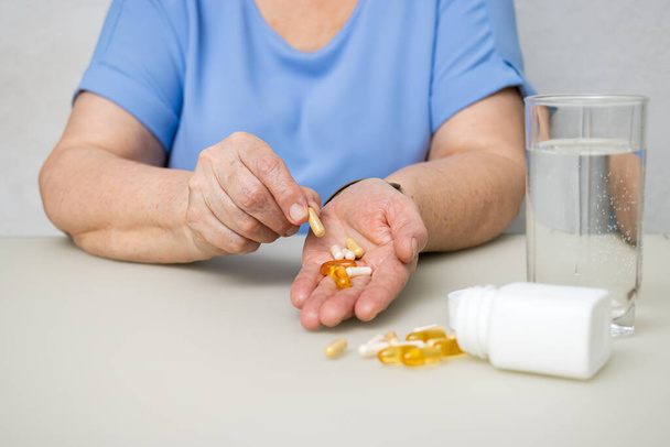 Starší žena s vrásčitýma starýma rukama u stolu, držící různé kapsle, vitamíny a pilulky na léčbu. Zdravotnictví a medicína koncepce. - Fotografie, Obrázek
