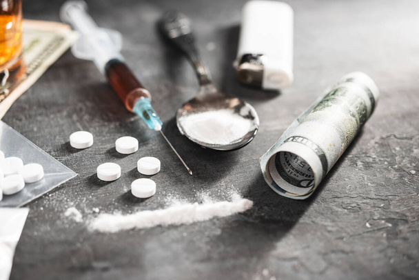 Weiße Pillen, Spritze mit einer Dosis Drogen, Betäubungspulver in einem Löffel und gerollte US-Dollar-Banknote auf dunklem Hintergrund. Konzept von Sucht und schlechten Gewohnheiten. - Foto, Bild