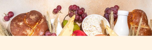 フード付きハッピーシャボーグリーティングカードの背景ユダヤ人のシャボーの休日のシンボル-ザクロ、ブドウ、リンゴ、甘いチャラパン、小麦スパイク、ミルク、チーズ、コテージチーズ、ベージュの背景 - 写真・画像