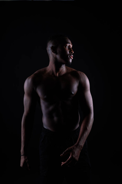 Портрет атлетичного афроамериканца без топа на черном фоне - Фото, изображение