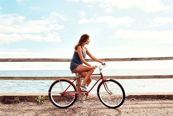 Fitness is a lifestyle. a beautiful young woman riding her bicycle on the promenade - Фото, изображение