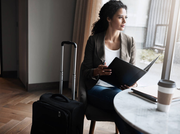 Soms moet je naar je doel reizen. een jonge zakenvrouw leest door een business folder terwijl ze wacht op haar vlucht in een luchthaven lounge - Foto, afbeelding