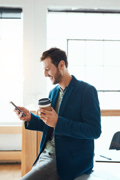 У него неформальный подход к бизнесу. красивый молодой бизнесмен, использующий свой мобильный телефон во время работы в современном офисе - Фото, изображение