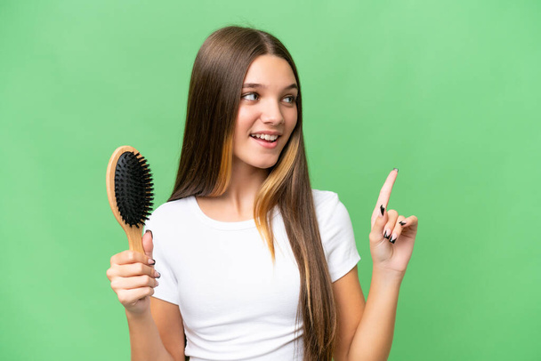 Nastolatka kaukaska dziewczyna z grzebieniem włosów na odizolowanym tle z zamiarem realizacji rozwiązania podczas podnoszenia palca w górę - Zdjęcie, obraz