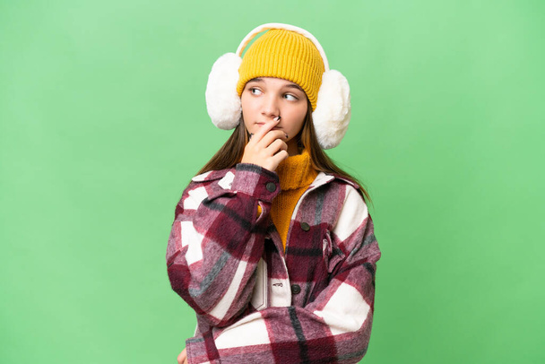 Έφηβος καυκάσιος κορίτσι φορώντας muffs χειμώνα πάνω από απομονωμένη φόντο έχουν αμφιβολίες και με συγκεχυμένη έκφραση προσώπου - Φωτογραφία, εικόνα