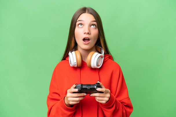Video oyunu kontrolörüyle oynayan beyaz bir kız izole edilmiş arka planda yukarı bakıyor ve şaşırmış bir ifadeyle - Fotoğraf, Görsel