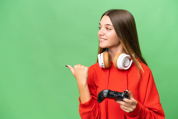 Teenager caucasian girl playing with a video game controller over isolated background pointing to the side to present a product - Foto, afbeelding
