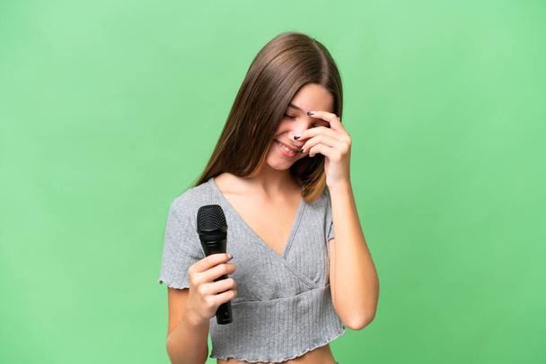 Teenager-Sängerin nimmt Mikrofon über isoliertem Hintergrund lachend in die Hand - Foto, Bild