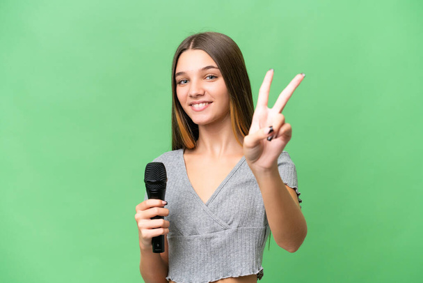ティーン歌手女の子ピックアップマイク上の隔離された背景笑顔とショーの勝利サイン - 写真・画像