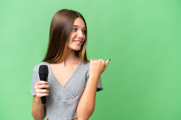Tini énekes lány felvesz egy mikrofon felett elszigetelt háttér mutatva az oldalra, hogy bemutassa a termék - Fotó, kép