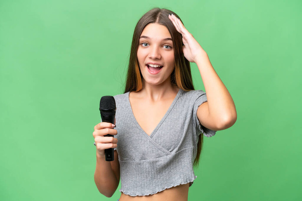 Teenager singer girl picking up a microphone over isolated background with surprise expression - 写真・画像