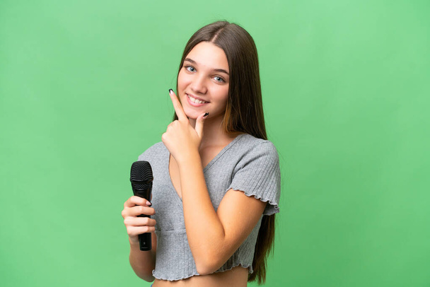 Genç şarkıcı kız izole edilmiş bir arka planda mikrofon tutuyor mutlu ve gülümsüyor. - Fotoğraf, Görsel
