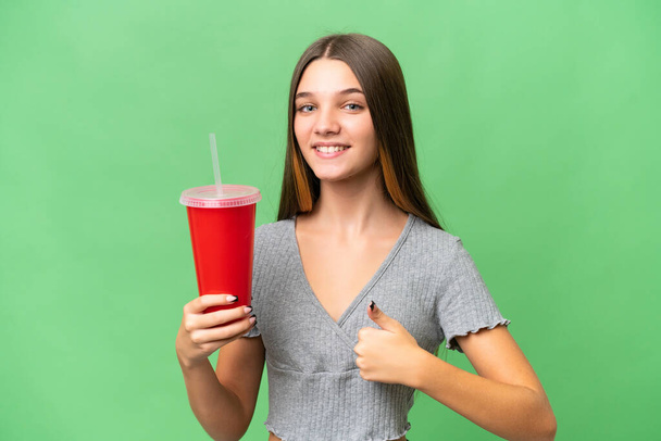 Nastolatka kaukaska dziewczyna trzyma napój na odosobnionym tle z kciukami w górze, bo stało się coś dobrego - Zdjęcie, obraz