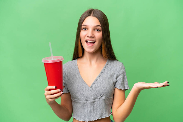 Teenager caucasian girl holding a soda over isolated background with shocked facial expression - 写真・画像