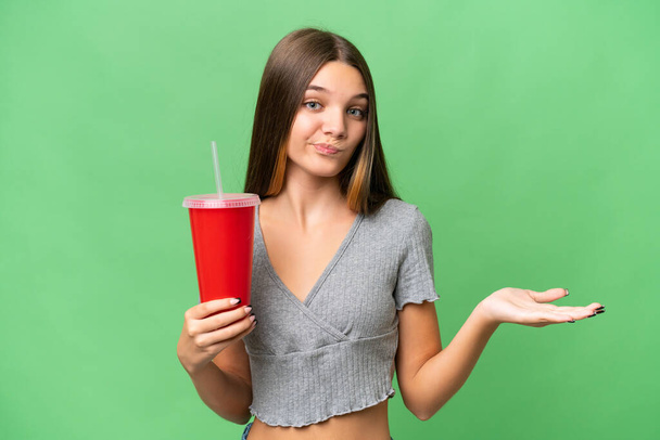 Nastolatka kaukaska dziewczyna trzyma napój na odosobnionym tle co wątpliwość gest podczas podnoszenia ramion - Zdjęcie, obraz
