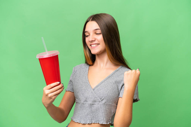 Adolescente caucásica chica sosteniendo un refresco sobre aislado fondo celebrando una victoria - Foto, imagen