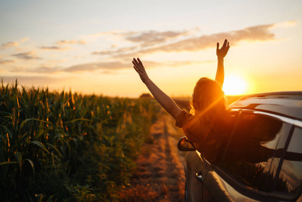 Young happy woman leaning out of the car window enjoying the sunset. The concept of active lifestyle, travel, tourism, nature. - Foto, imagen