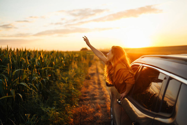 Young happy woman leaning out of the car window enjoying the sunset. The concept of active lifestyle, travel, tourism, nature. - Φωτογραφία, εικόνα