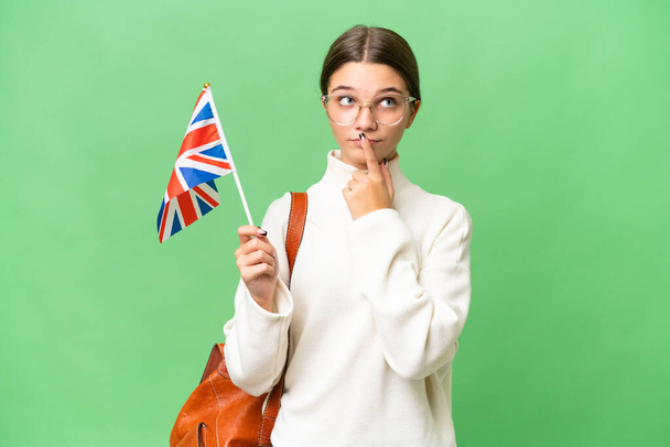 Kafkas kökenli genç bir kız, izole edilmiş arka planda Birleşik Krallık bayrağı taşıyor. - Fotoğraf, Görsel
