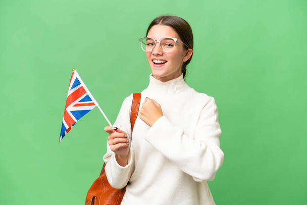 Adolescente estudante caucasiano menina segurando uma bandeira do Reino Unido sobre fundo isolado celebrando uma vitória - Foto, Imagem