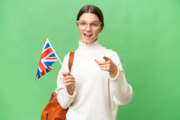 Teenager Student kaukasische Mädchen mit einer britischen Flagge über isoliertem Hintergrund überrascht und zeigt nach vorne - Foto, Bild