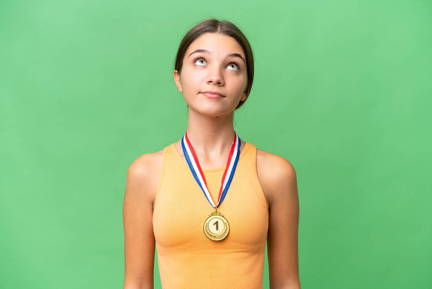 Adolescente caucasienne fille avec des médailles sur fond isolé et regardant vers le haut - Photo, image