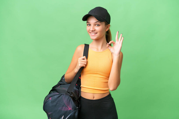adolescente caucásico chica con bolsa de deporte sobre aislado fondo mostrando ok signo con los dedos - Foto, imagen