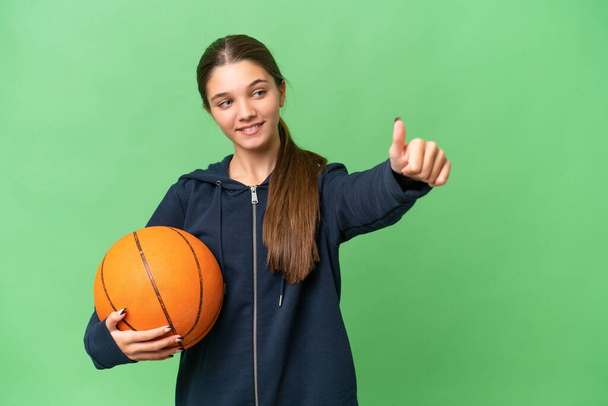 Девушка-кавказка-подросток играет в баскетбол на изолированном фоне, показывая большой палец вверх. - Фото, изображение