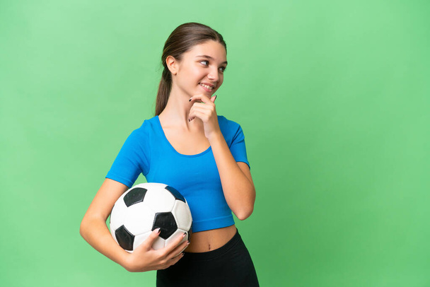 Teenager caucasian girl playing football over isolated background thinking an idea and looking side - Foto, Imagem