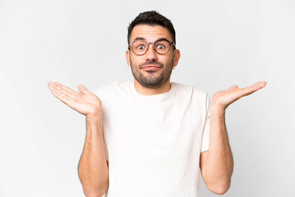 Young handsome caucasian man over isolated white background making doubts gesture - Foto, afbeelding