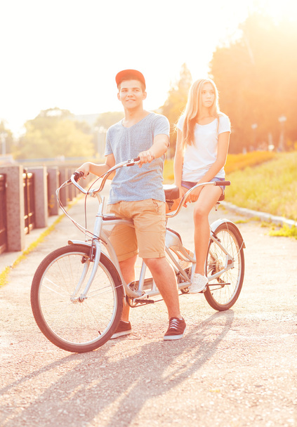 Young man and woman riding a bicycle in the park outdoors - Fotoğraf, Görsel