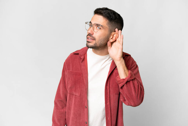 Jeune homme caucasien beau sur fond blanc isolé écoutant quelque chose en mettant la main sur l'oreille - Photo, image